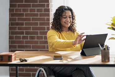 Woman in wheelchair sitting at a desk working on a tablet