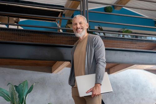 A casual Gen X businessman descends an office staircase with his laptop.
